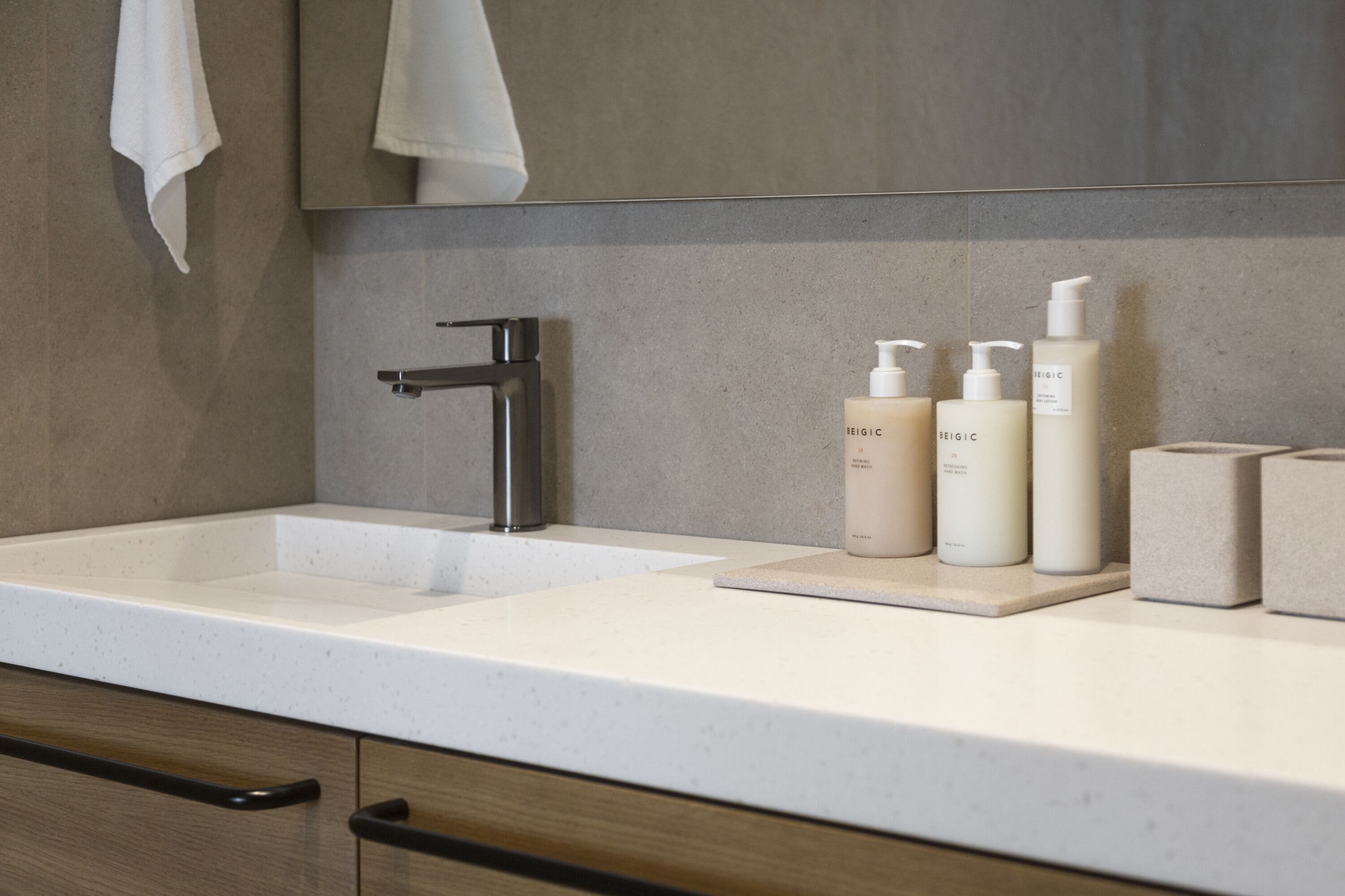 Un bagno con un lavandino moderno, uno specchio e tre flaconi di articoli da toilette sul ripiano.