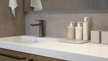 Un bagno con un lavandino moderno, uno specchio e tre flaconi di articoli da toilette sul ripiano.