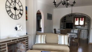Ein Wohnzimmer mit Kamin, einer Couch, einem Essbereich und einer durch einen Bogen sichtbaren Küche.