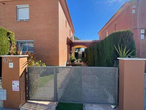 A residential building with a gated entrance, a small garden, and a clear blue sky.