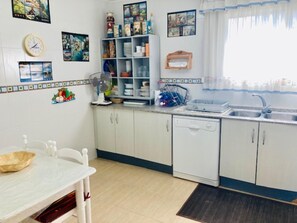 Une cuisine avec des meubles blancs, un lave-vaisselle, un évier et un ventilateur. Les murs sont décorés et il y a un calendrier.