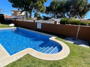A swimming pool with a curved edge, surrounded by a brick wall and a grassy area.