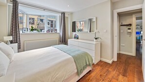 A bedroom with a large bed, a dresser, a mirror, and a window with curtains.