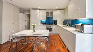 A modern kitchen with white cabinets, a central island with chairs, and a microwave on the countertop.