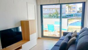 A modern living room with a flat-screen TV, a dark-colored sofa, and a large sliding glass door leading to an outdoor area with a pool and chairs. - Ground Floor Apartment with Pool Access Near Beach in Miami Playa (Miami Playa)