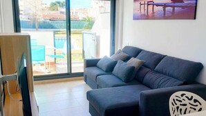 A living room with a grey sofa, a flat-screen TV, and a painting of a sunset over water. - Ground Floor Apartment with Pool Access Near Beach in Miami Playa (Miami Playa)
