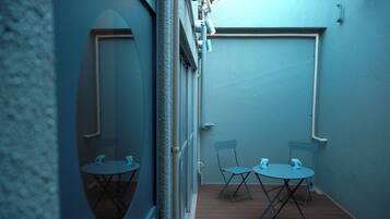 A narrow corridor with a wooden floor, two folding chairs, and two small round tables, each with a mug.