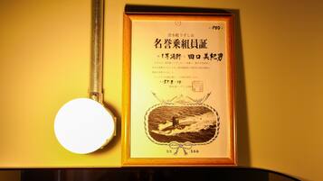 Un certificado enmarco con texto en japonés e ilustración de un barco, colgado en una pared junto a un espejo redondo.
