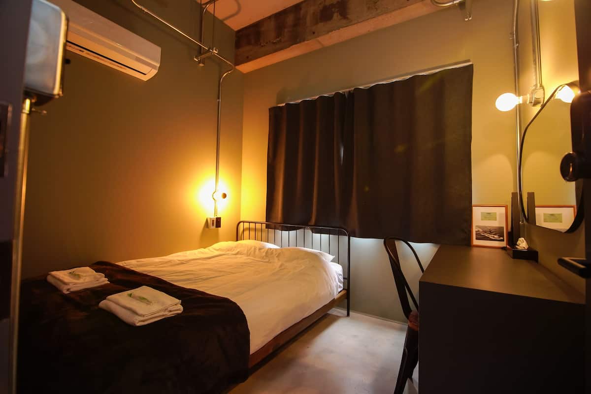 A bedroom with a bed, bedside table, lamp, air conditioning unit, and a window with curtains.
