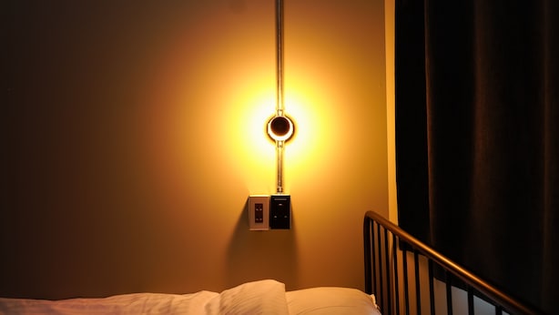 Una cama con cabecera, una lámpara de pared y un enchufe.