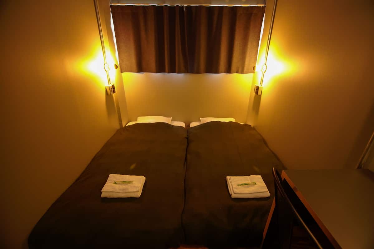 A twin bed with two towels, a window with curtains, and wall-mounted lights.