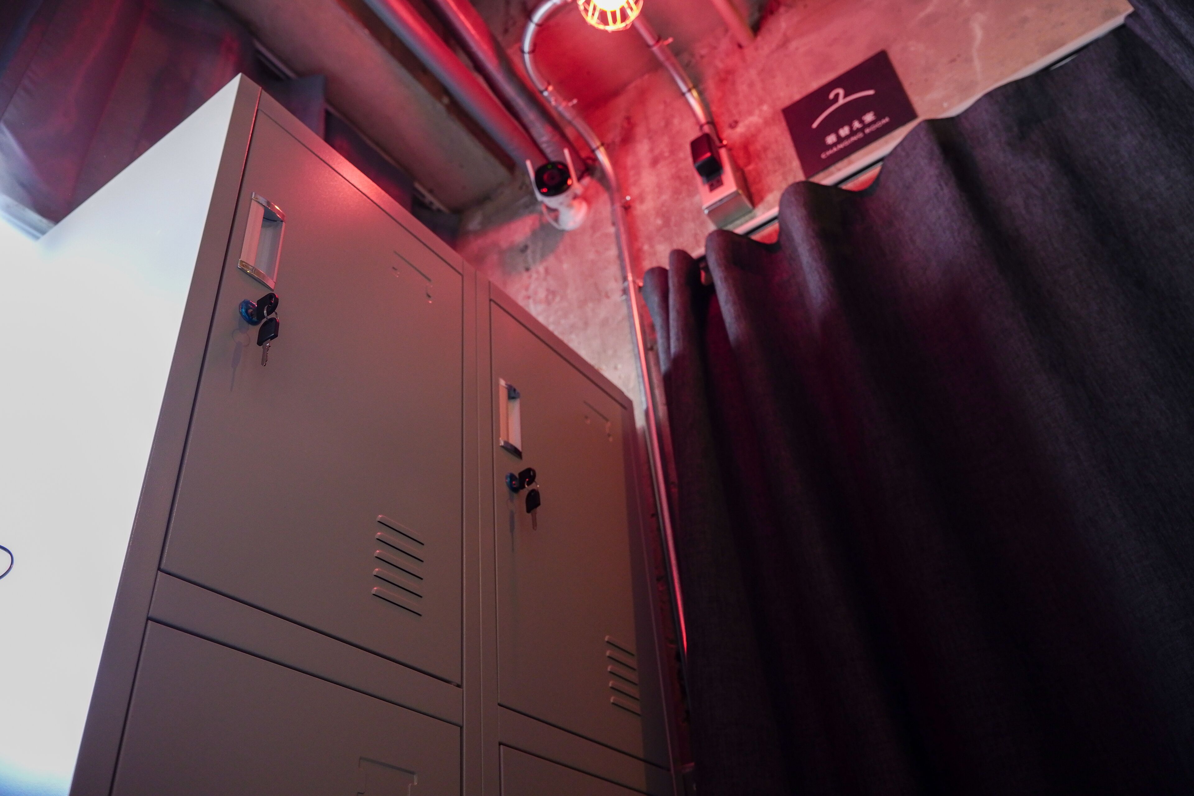 A locker room with metal lockers, a red light fixture, and a black curtain.
