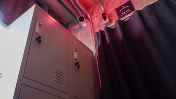 A locker room with metal lockers, a red light fixture, and a black curtain.
