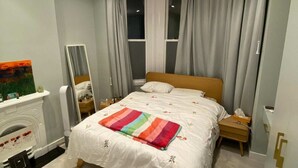 Ein modernes Schlafzimmer mit einem großen Bett, einem Nachttisch, einem Spiegel und einem Kamin.