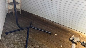 Ein Holzboden mit einem schwarzen Metallstuhl und einer Holzleiter, die an einer weißen Wand mit horizontalen Linien anlehnt.
