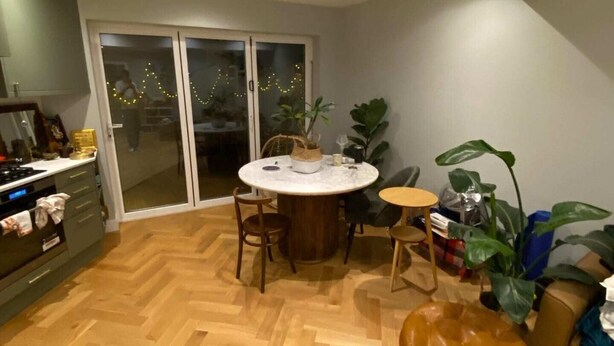 Eine moderne Küche mit Fischgrätparkett, einem Essbereich mit rundem Tisch und einer Glastür zum Balkon.