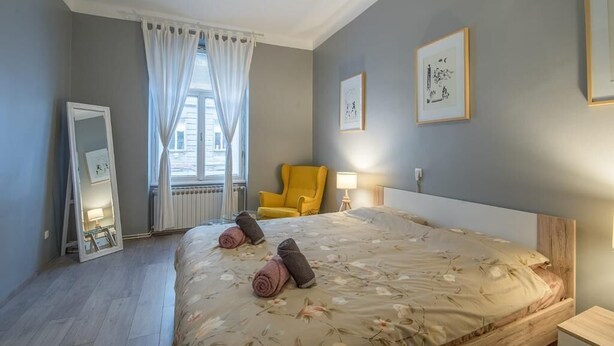 Una habitación de hotel con cama, una silla, un espejo y obras de arte en las paredes.
