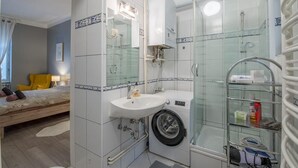 Un baño pequeño con cabina de ducha de vidrio, lavadora y lavamanos.