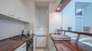 Cocina moderna con armarios blancos, encimera de madera, estufa a gas, hervidor y ventana con persianas.