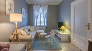 Un espacio habitable compacto con un sofá, una mesita, una silla, un escritorio con lámpara, un televisor y una puerta.