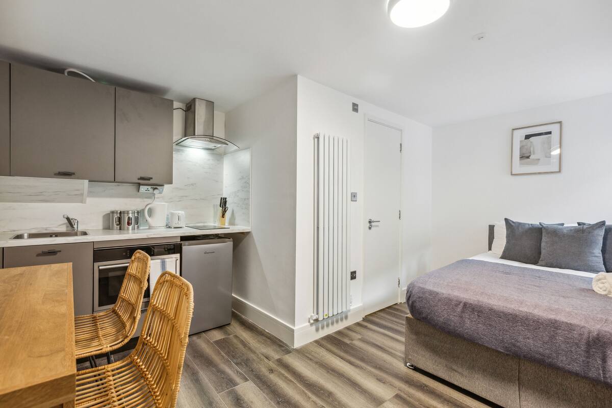 Quarto de hotel compacto com cama, pequena cozinha, área de refeições com mesa e cadeiras, e banheiro.