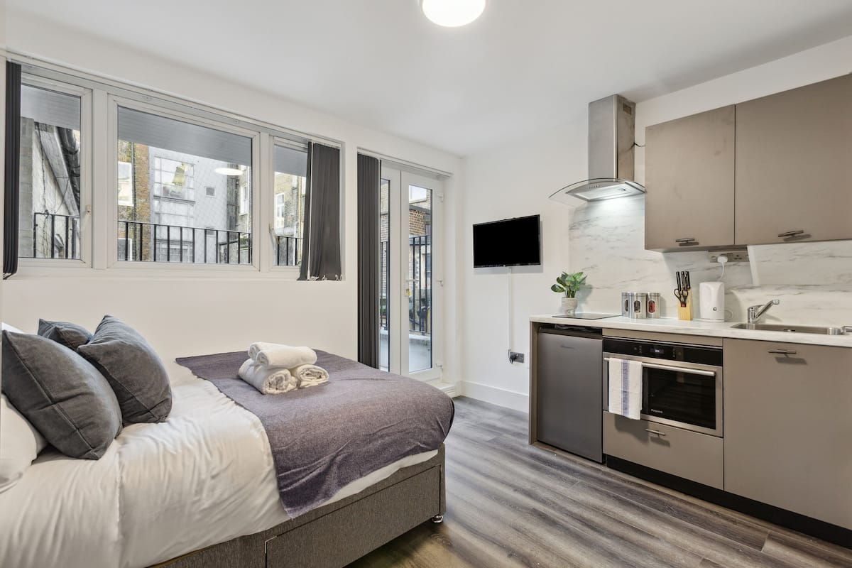Quarto moderno com cama, mesa de cabeceira, janela com cortinas e vista para o exterior.