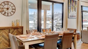 Un coin repas avec une grande fenêtre donnant sur un paysage montagneux enneigé.