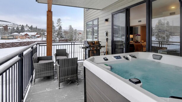 Un balcon doté d’un jacuzzi, de fauteuils en osier et offrant une vue sur un paysage enneigé.
