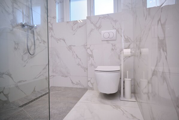 A modern bathroom with a glass-enclosed shower, a toilet, and a marble-tiled wall. - LaMer Luxury Suite by Litto (Split)