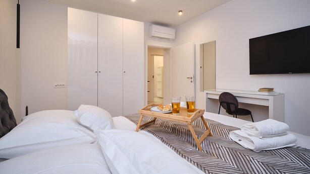 Quarto de hotel com uma cama, uma escrivaninha com cadeira, uma televisão e um tabuleiro com itens de café da manhã.