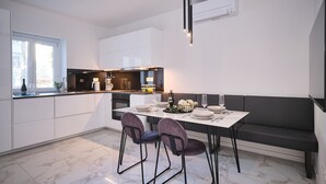 Uma cozinha moderna com armários brancos, piso de mármore e um espaço de jantar com bancos e cadeiras.