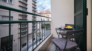 Uma varanda com mesa e cadeiras, uma tigela de frutas e vista para um edifício com grafites.