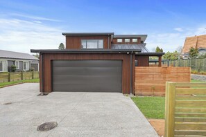 A modern two-story house with a garage, a wooden fence, and a paved driveway. - Inn Sophia - Two Homes, Spa Pools, Sleeps 10 (Rotorua)