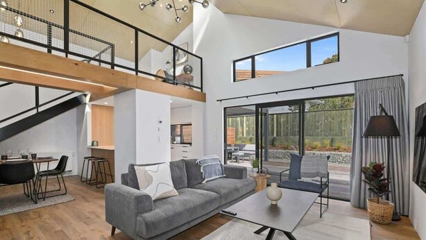 A spacious living area with a grey sofa, a coffee table, and a staircase leading to an upper level. - Inn Sophia - Two Homes, Spa Pools, Sleeps 10 (Rotorua)