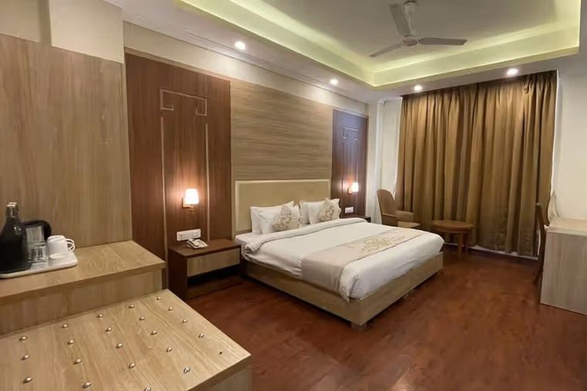 A hotel room with a bed, bedside tables, a TV, a ceiling fan, and a window with curtains.