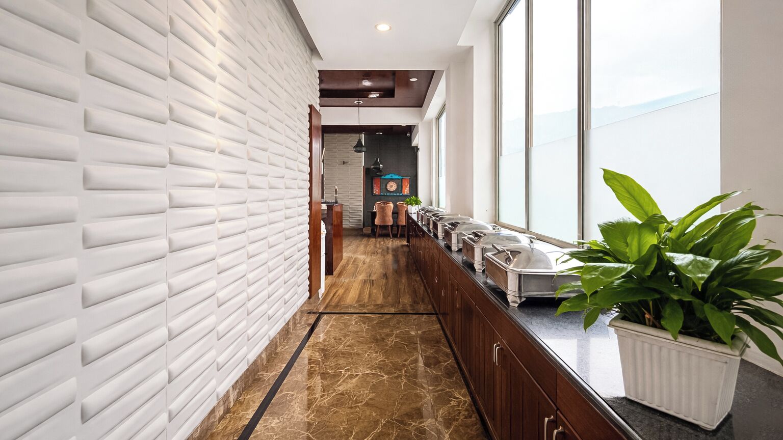A hallway with a white textured wall, a marble floor, and a long counter with food service items.