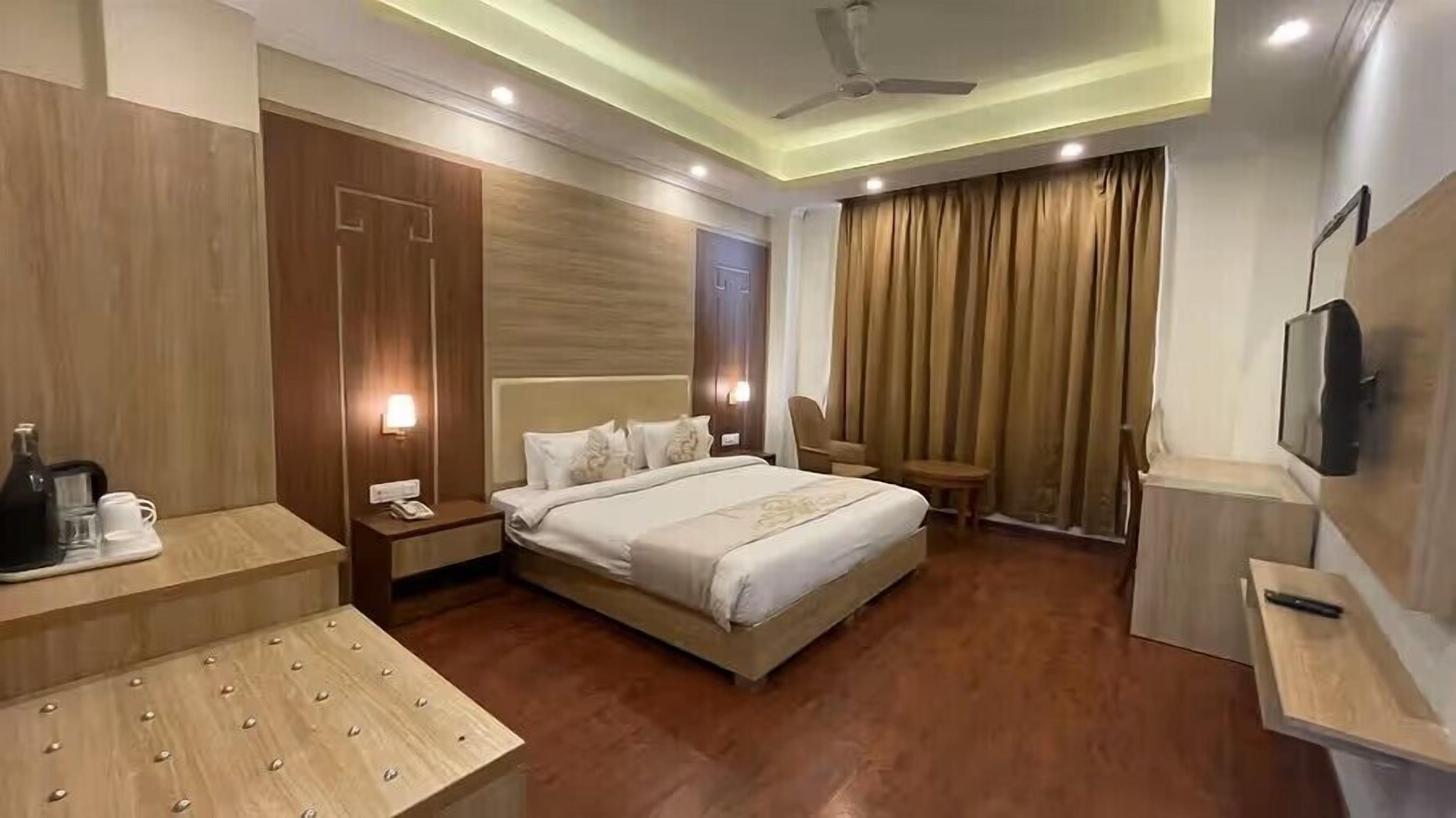 A hotel room with a bed, bedside tables, a TV, a ceiling fan, and a window with curtains.