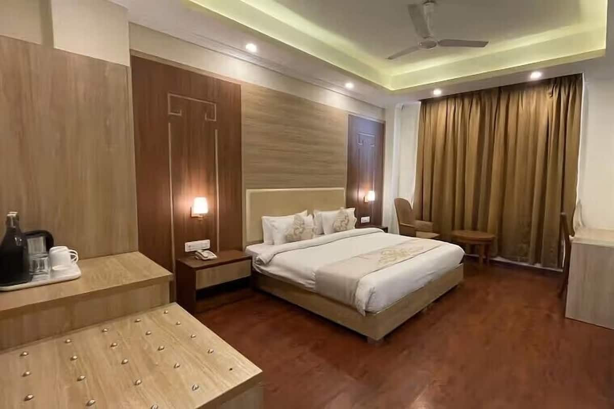 A hotel room with a bed, bedside tables, a TV, a ceiling fan, and a window with curtains.