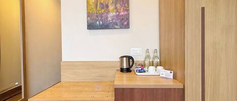 Habitación de hotel con un escritorio de madera, un cuadro en la pared, un hervidor, botellas y una bandeja con una taza y una bolsita.