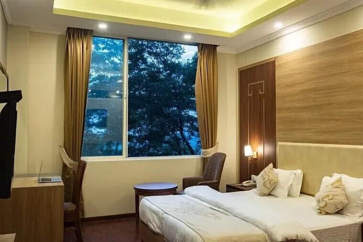 Ein Hotelzimmer mit Bett, Schreibtisch, Stuhl, einem Fenster mit Vorhängen und einem Nachttisch mit Lampe.