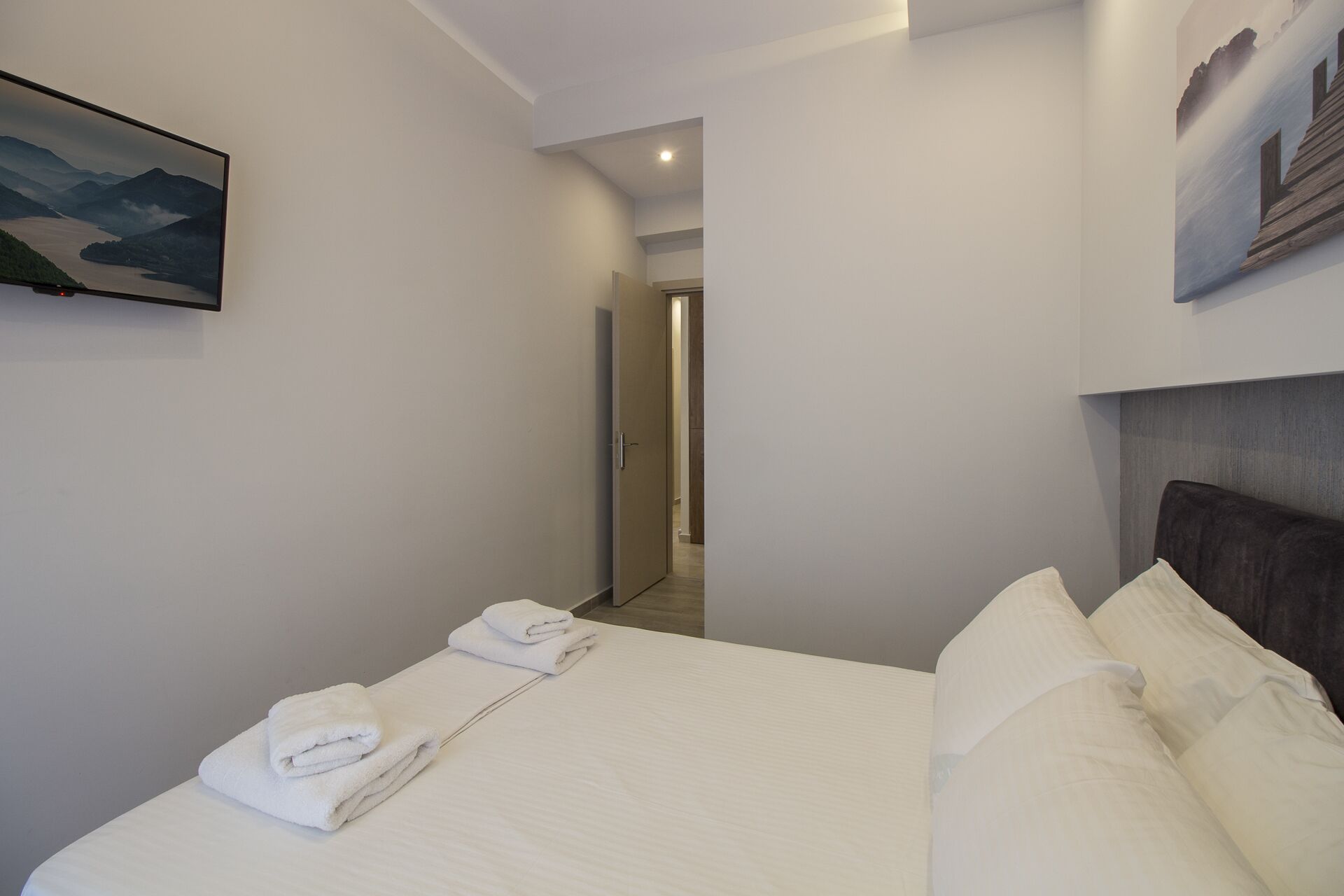 A hotel room with a neatly made bed, a painting on the wall, and a view of a mountain landscape.