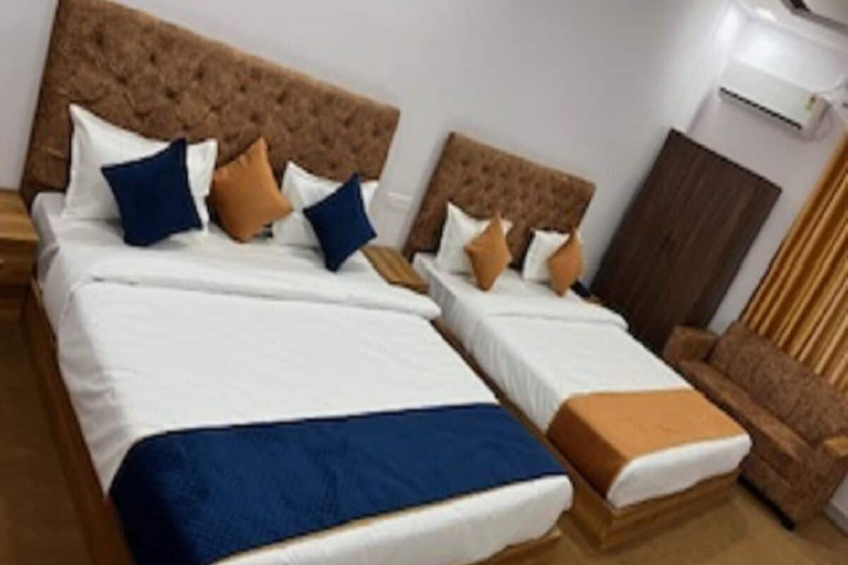 Ein Hotelzimmer mit zwei Betten, jeweils mit brauner Kopfteil, weißer Bettwäsche und mehreren Kissen in Blau und Braun.