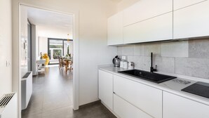 A modern kitchen with white cabinets, a black sink, and a countertop with a kettle and coffee maker. - 3670 Villa Perlaianca by Perle di Puglia (Carovigno)