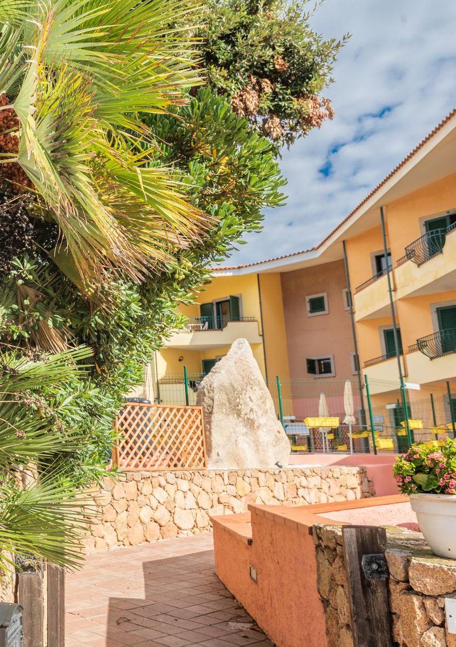 A courtyard with a stone wall, a large rock, and a building with balconies.