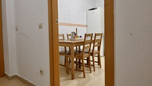 A dining area with a wooden table and chairs, a white refrigerator, and a tiled backsplash.