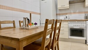 A kitchen with a wooden dining table, chairs, a refrigerator, an oven, and a coffee maker.