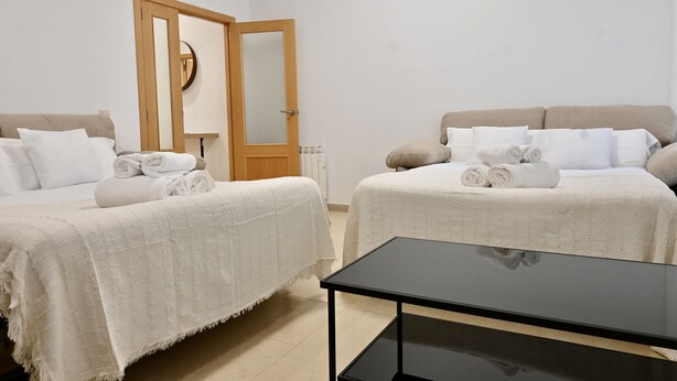 A hotel room with two beds, a wooden door, a black table, and a white wall.