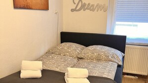 A neatly made bed with a dark headboard, patterned bedding, and two folded towels. A world map and a 'Relax Dream' sign are visible on the walls. - Lovely 1-bed Apartment in Koblenz (Koblenz)