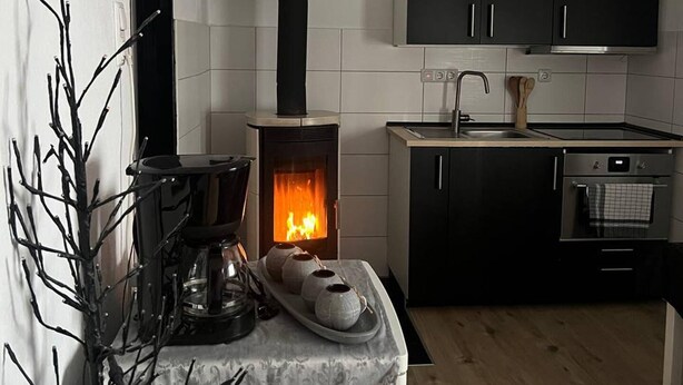 A modern kitchen with a wood-burning stove, black cabinets, and a small dining area. - Lovely 1-bed Apartment in Koblenz (Koblenz)