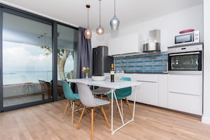 Uma cozinha moderna com vista para o mar, uma área de jantar com cadeiras cor turquesa e uma grande janela.